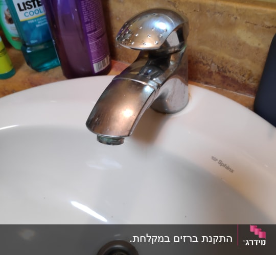 ברז כרום מעל כיור לבן עם ניקוז מתכת